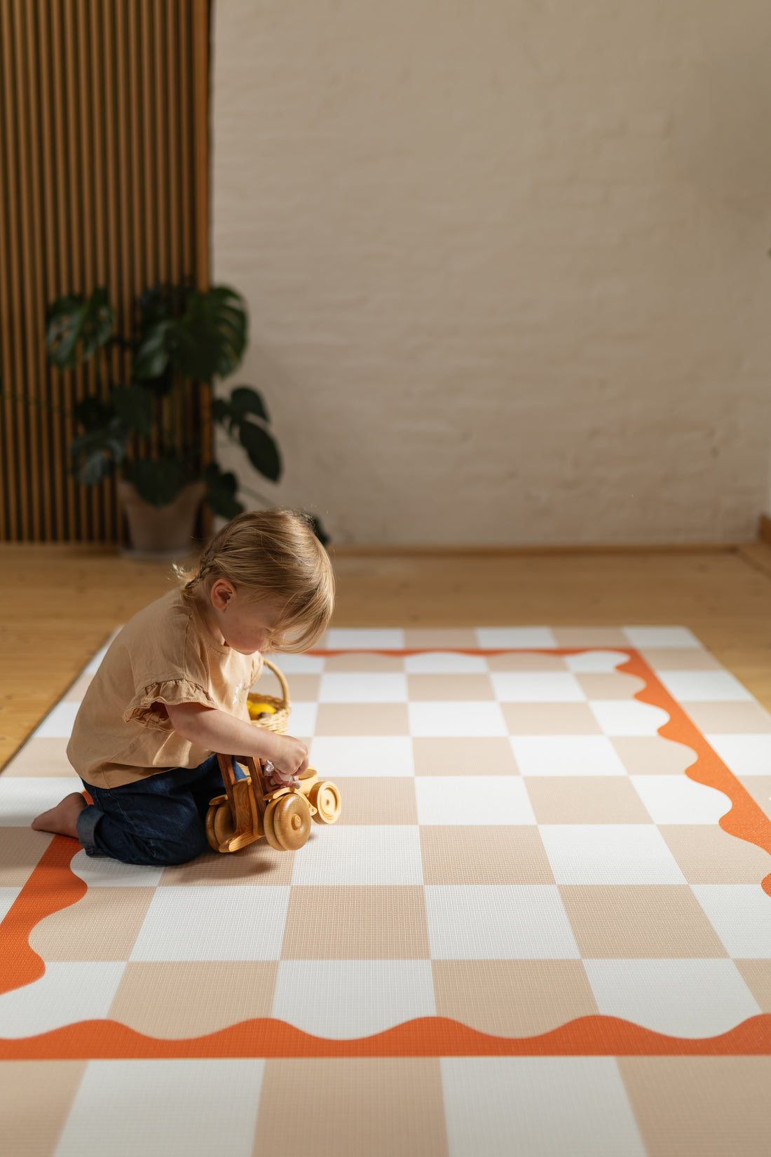 Play magic Child playing with a toy on a checkered floor mat in a room with a plant in the background.