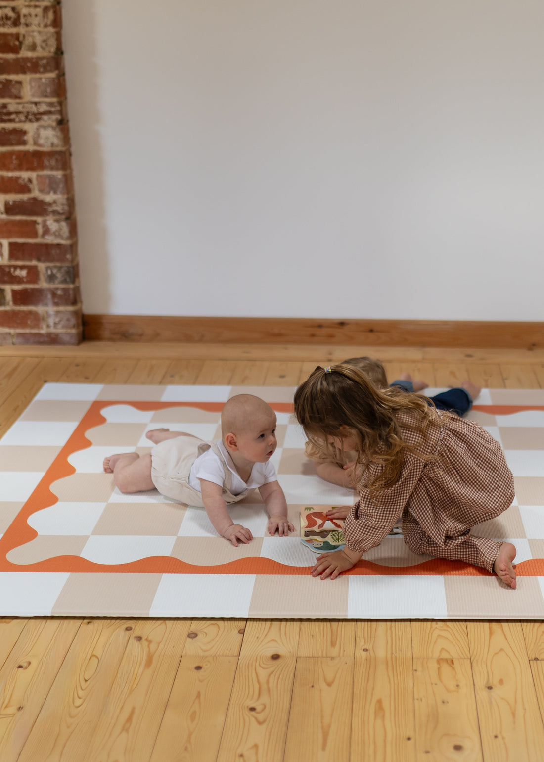 Reading time children playing on a colorful play mat in a room with wooden flooring and brick walls.