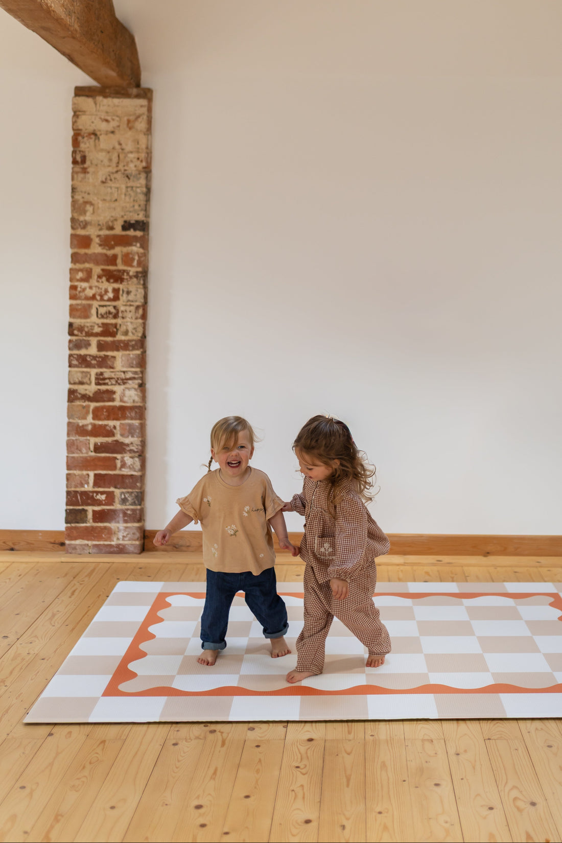Little giggles Having fun two children playing on a checkered playmat in a room with wooden floors and brick walls.