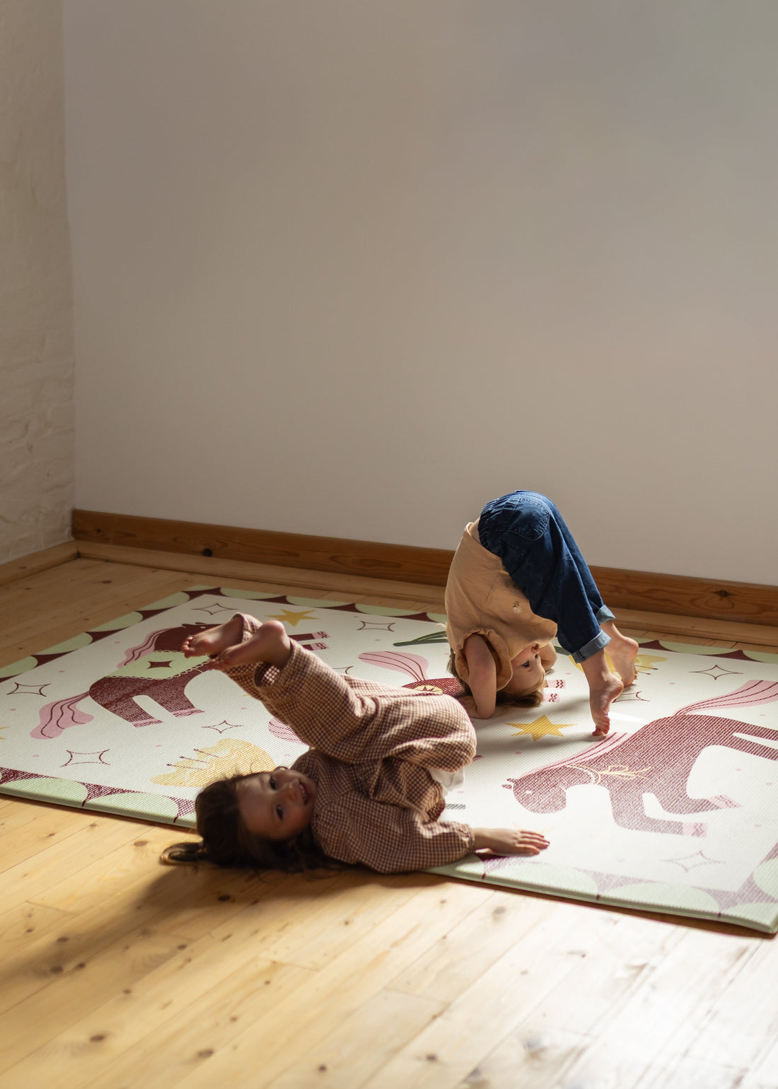 Rolly &Rolls Two children playing on a playmat with horse prints in a room with wooden flooring and white walls.