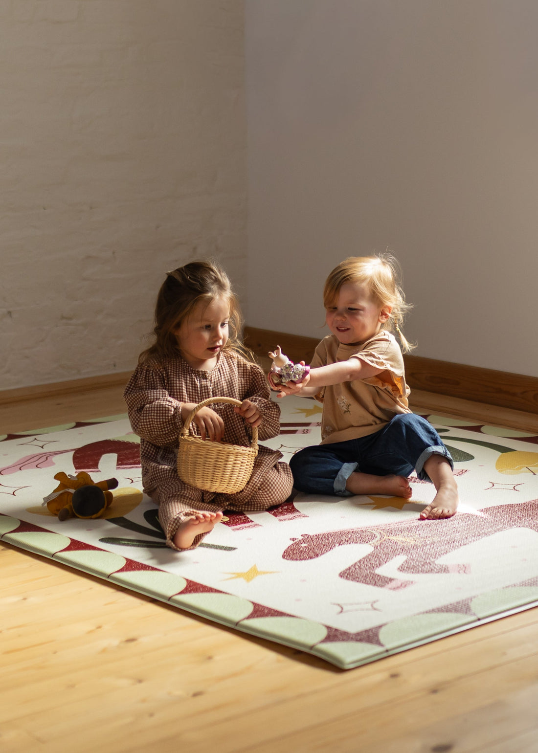Play time Two children playing on a playmat with toys in a room with wooden flooring and white walls.