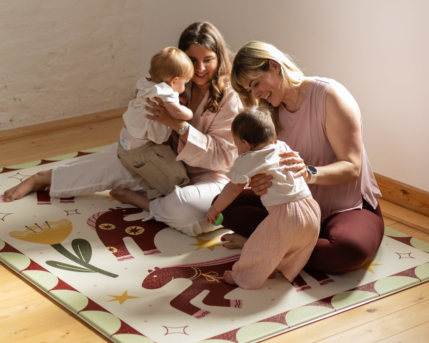 Mums with babies sitting on a colorful play mat smiling and interacting.